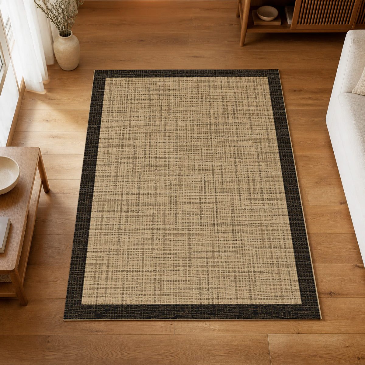 Kartela Jute Frame washable jute-look bordered area rug in Natural Black, on a wooden floor in a bright living room