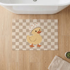 Kartela Duck Check washable checkered duck bath mat in Beige, on a wooden floor in front of a bathtub